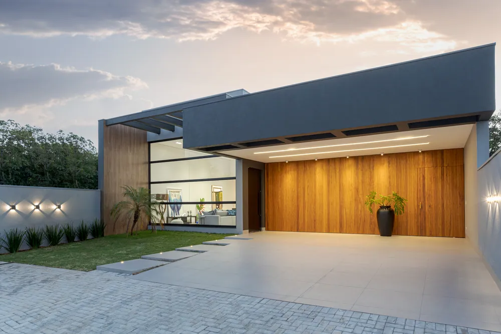 Fachada de casa residencial ao entardecer, com painel de madeira e iluminação acesa